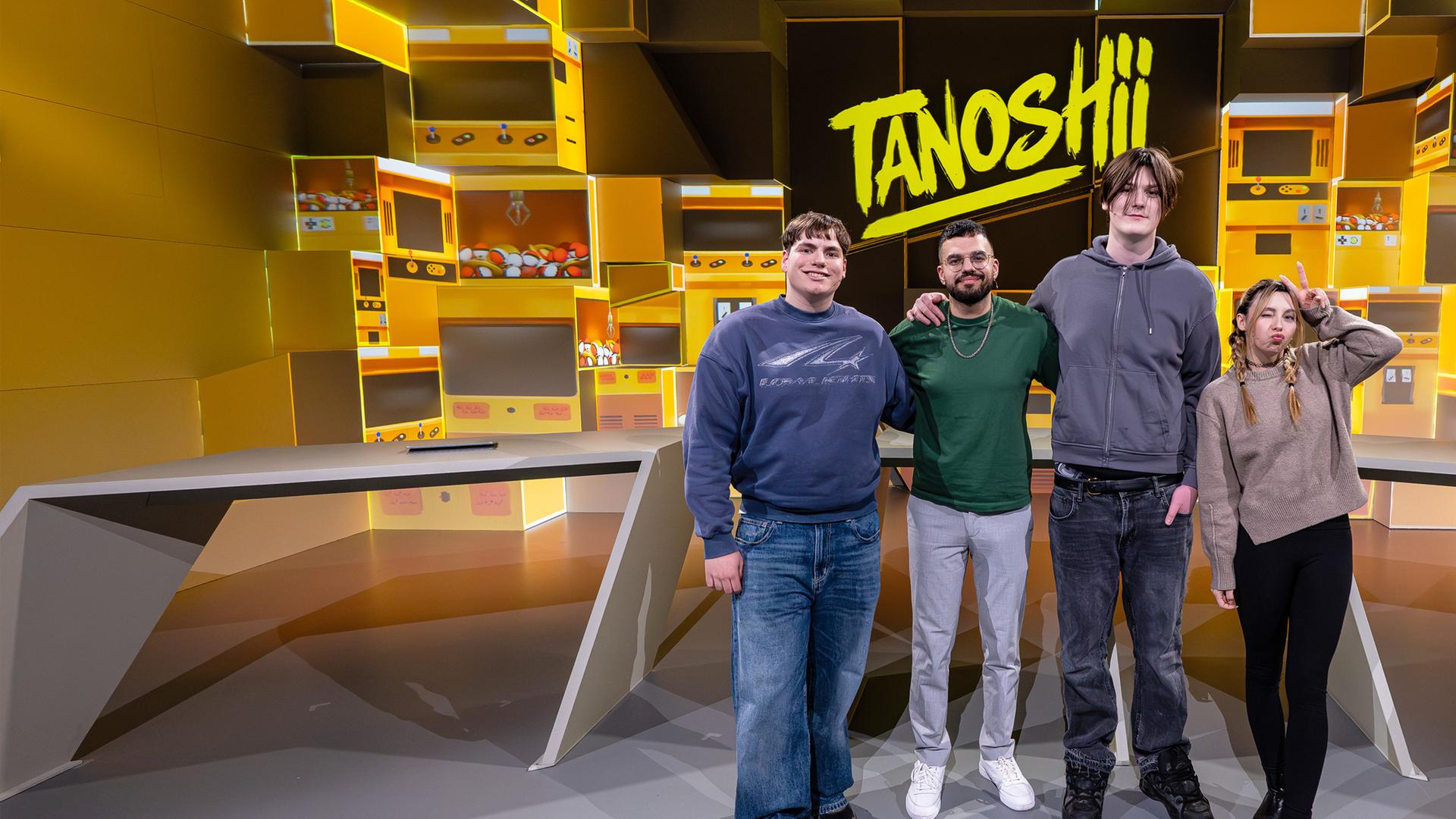 Vor der gelb gefärbten Studiokulisse stehen Arm in Arm v. l. n. r. Leonard, Cegi, Julien und JenNyan. Alle vier lächeln in die Kamera. Mittig über ihnen ist das Tanoshii-Logo zu sehen.