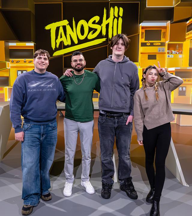 Vor der gelb gefärbten Studiokulisse stehen Arm in Arm v. l. n. r. Leonard, Cegi, Julien und JenNyan. Alle vier lächeln in die Kamera. Mittig über ihnen ist das Tanoshii-Logo zu sehen.