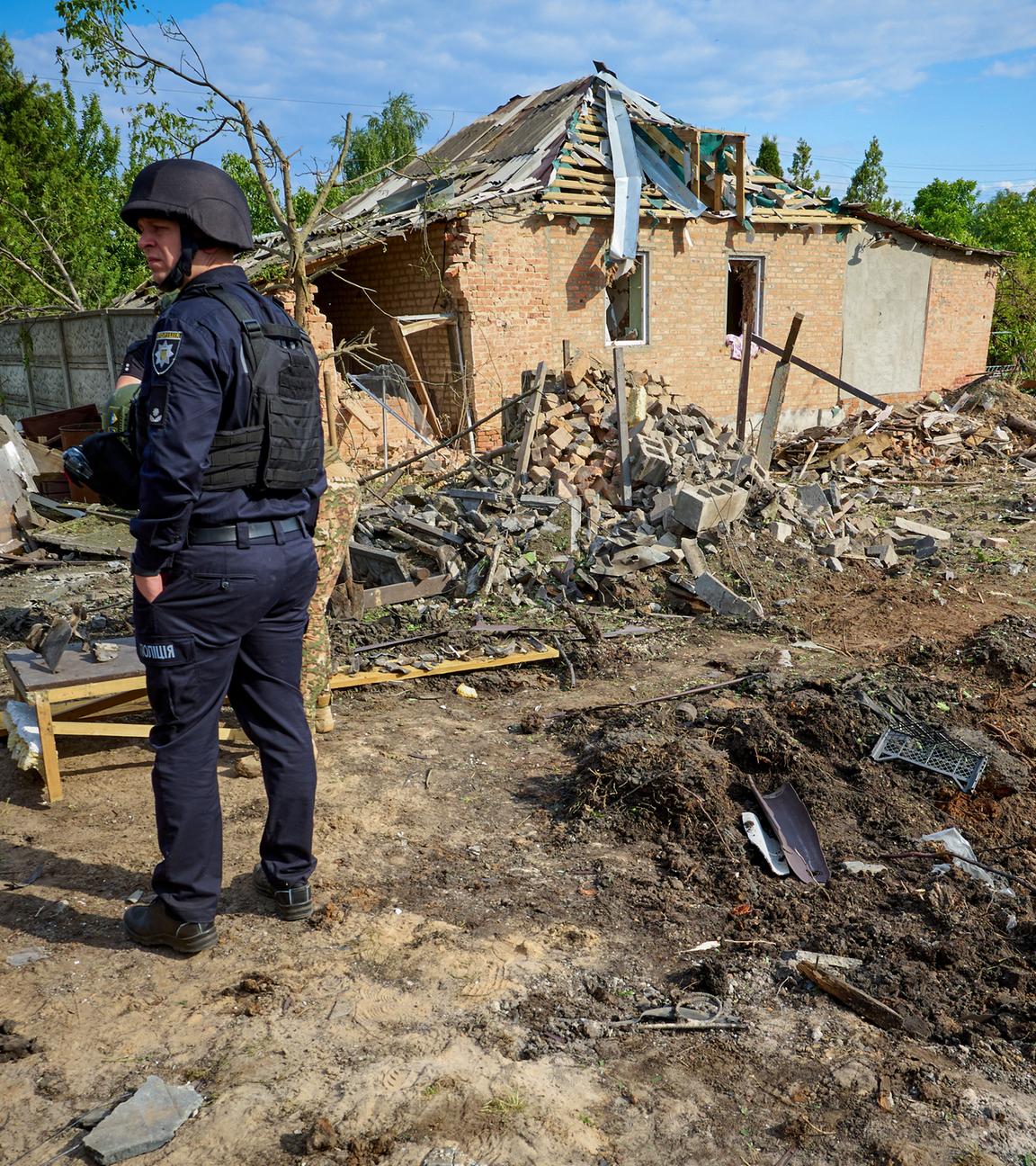 Ein Mann in Schutzuniform steht vor einem zerbombten Haus