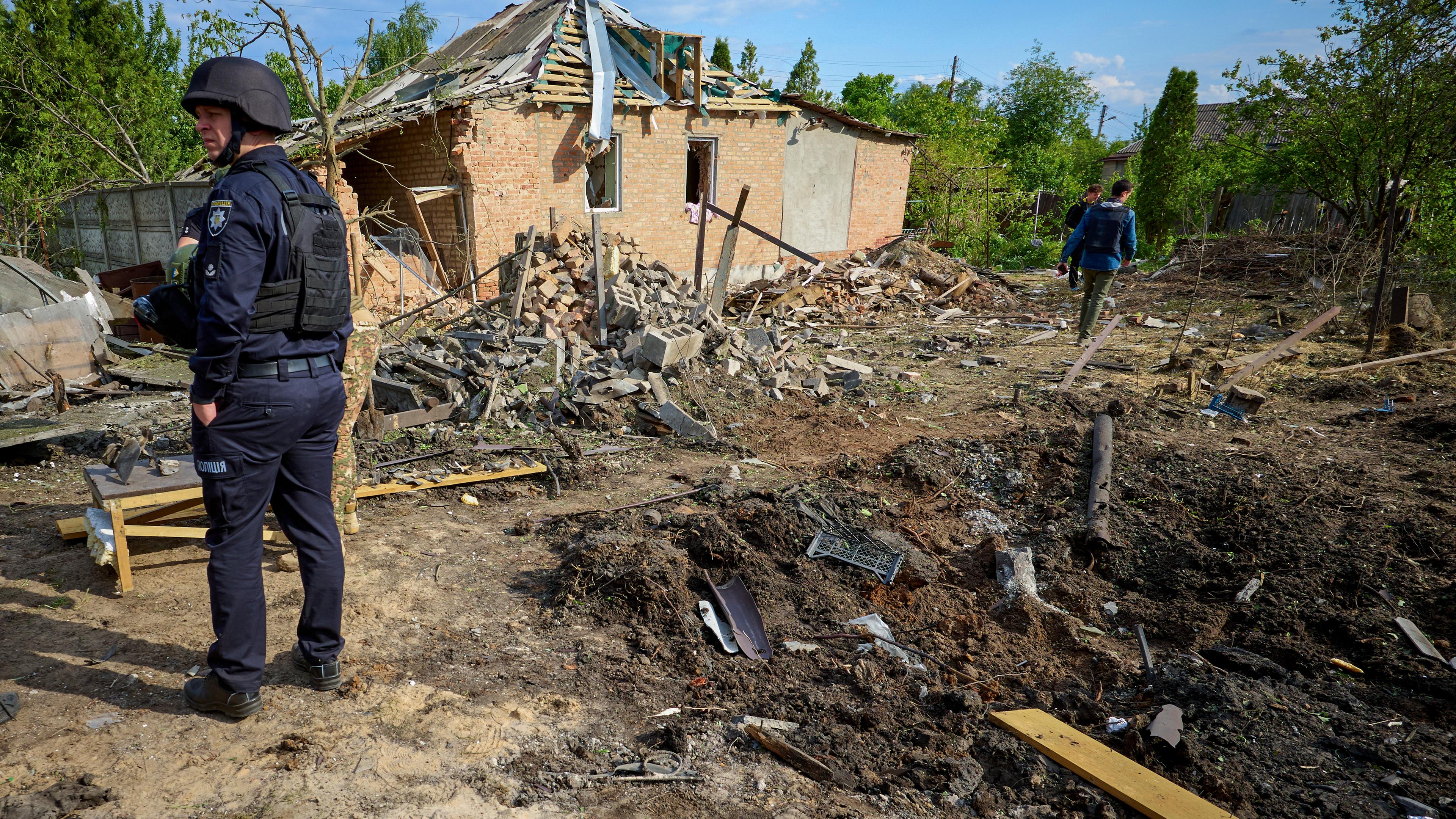 Ein Mann in Schutzuniform steht vor einem zerbombten Haus