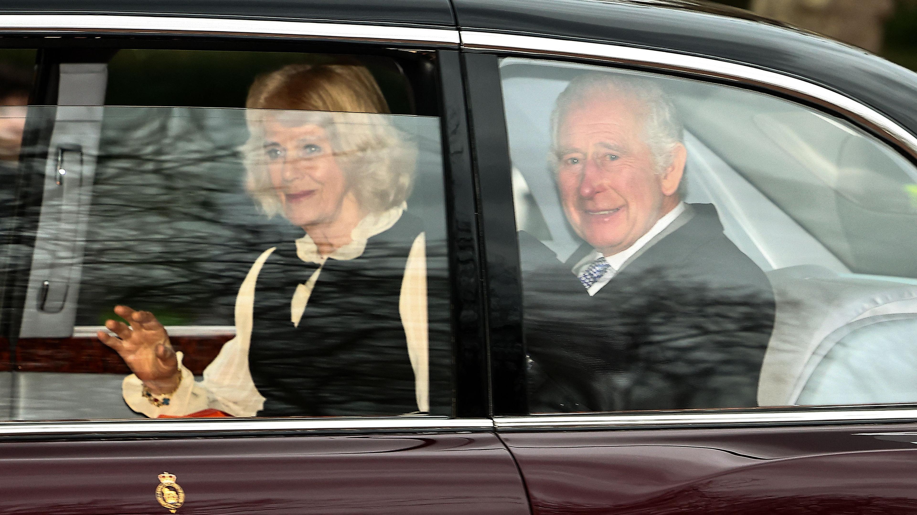 König Charles III. und Königin Camilla nach dem Treffen mit Prinz Harry. Das Königspaar wirkt guter Dinge und winkt den wartenden Menschen zu.
