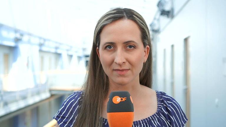 ZDF-Reporterin Charlotte Greipl schaut in die Kamera und hält ein Mikrofon in der Hand.