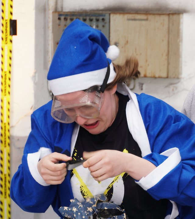 Zwei Jugendliche in blauen Weihnachtskostümen und Sicherheitsbrillen packen Geschenke ein.