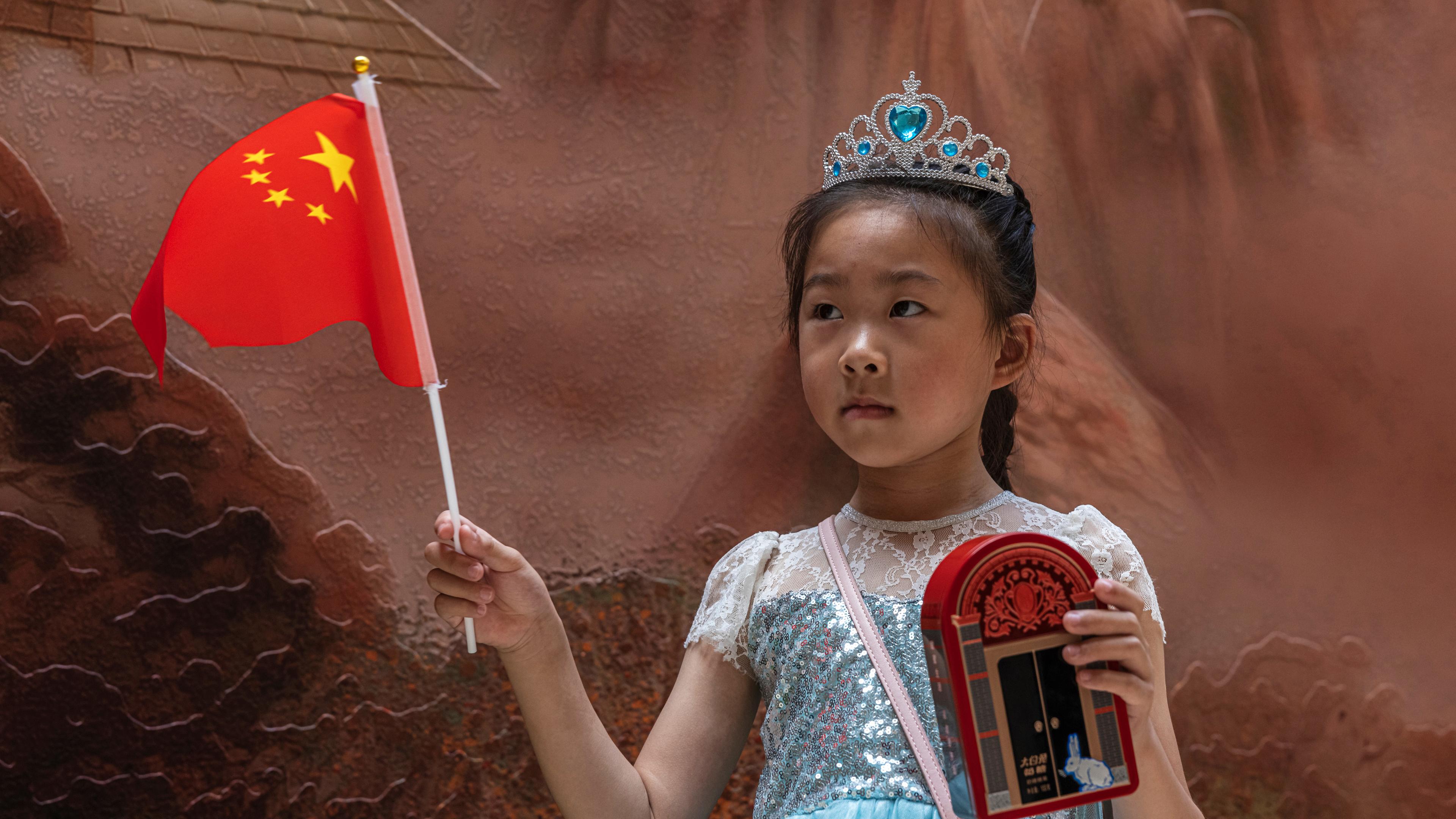 Ein chinesisches Mädchen im Prinzessinnenkleid hält einen Wimpel in den Farben der chinesischen Fahne hoch.