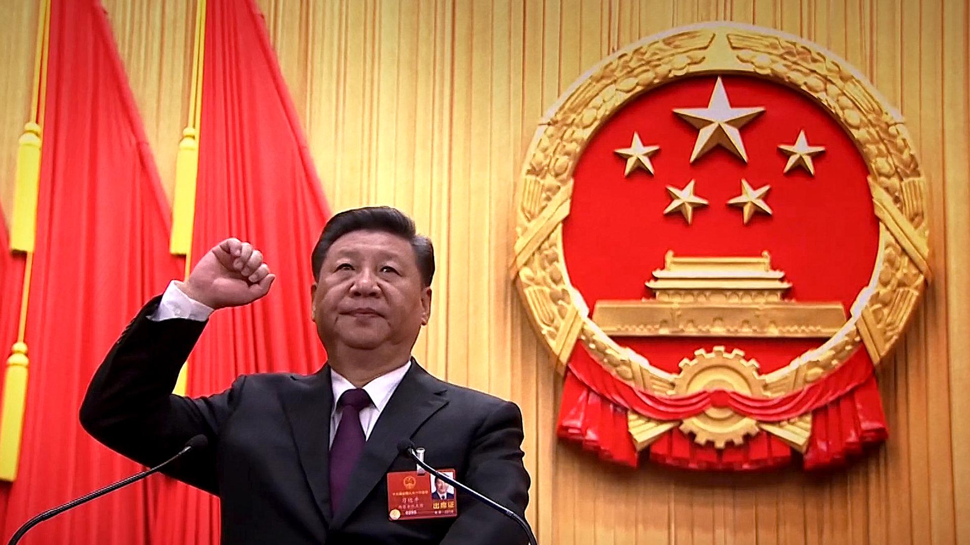 "China - Der entfesselte Riese - Präsident auf Lebenszeit": Xi Jinping steht mit erhobener Faust vor einem Rednerpult und dem nationalen Wappen der Volksrepublik China.