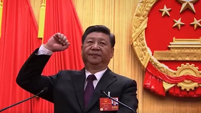 "China - Der entfesselte Riese - Präsident auf Lebenszeit": Xi Jinping steht mit erhobener Faust vor einem Rednerpult und dem nationalen Wappen der Volksrepublik China.