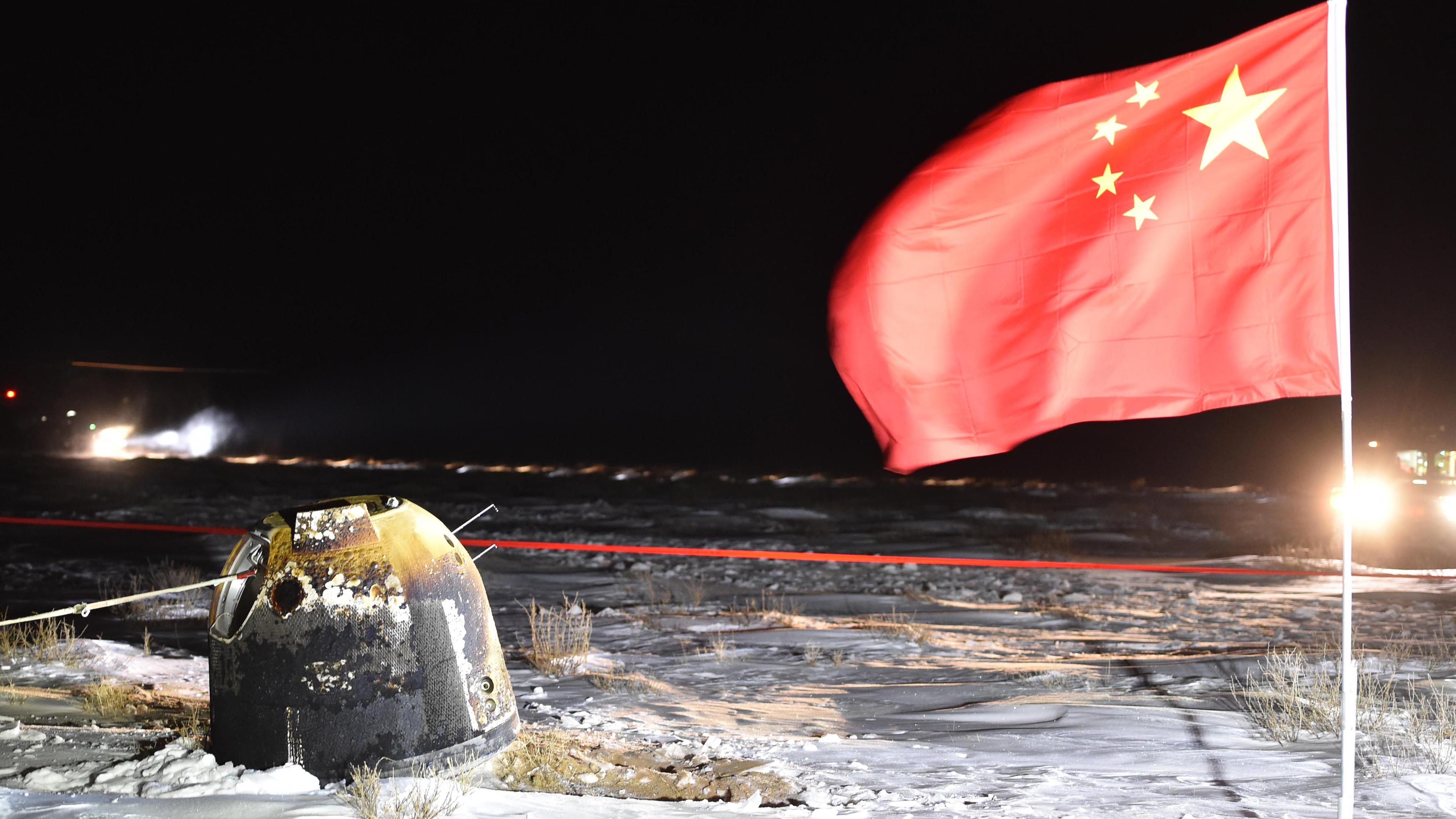 Auf dem Bild sieht man die Mondkapsel "Chang'e 5", die nach ihrer Mondmission mit Mondproben auf chinesischem Boden gelandet ist. Rechts daneben steckt eine chinesische Flagge im Boden. 