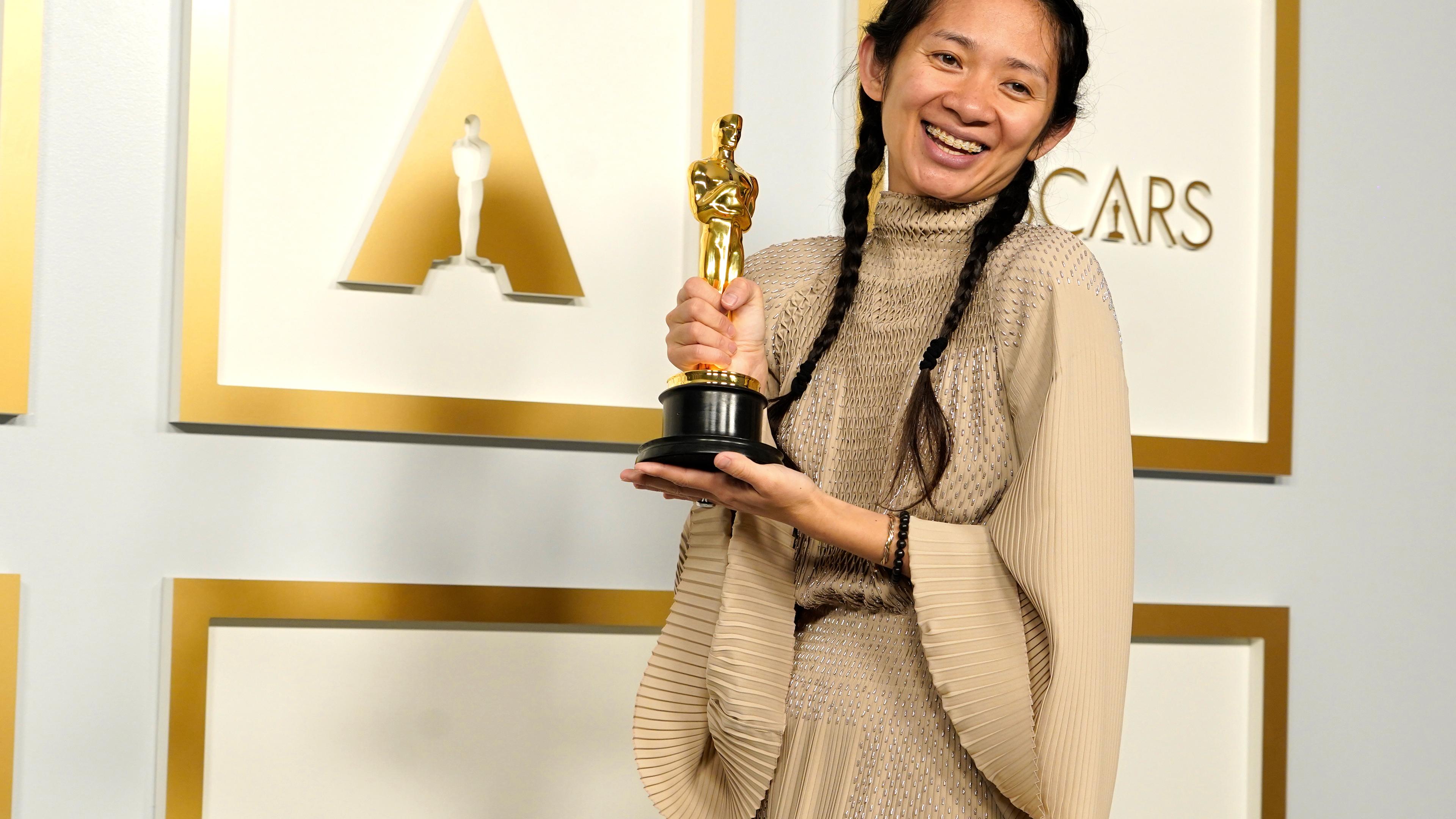 Eine junge chinesische Frau in einem golden glänzenden Kleid hält lachend eine goldene Oscar-Statue.