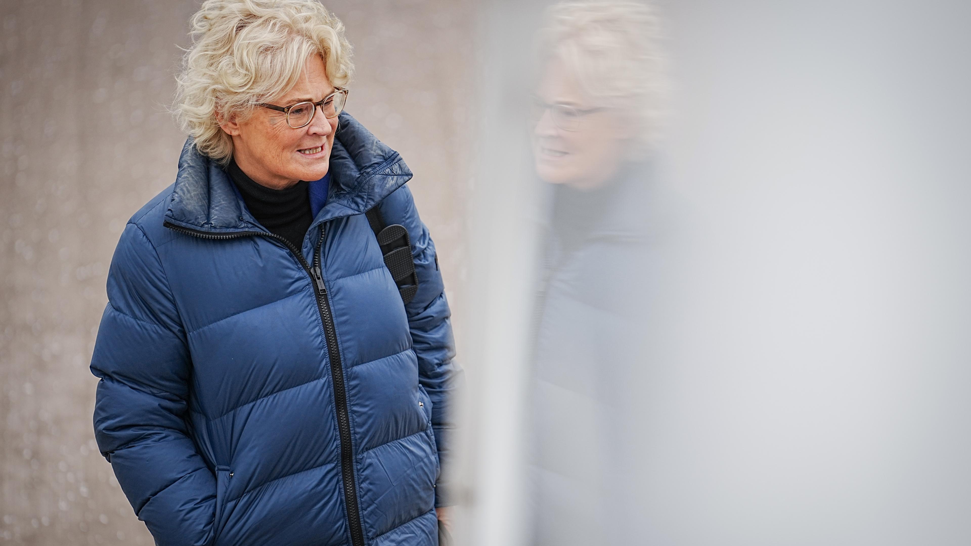 Christine Lambrecht (SPD), Bundesministerin der Verteidigung, läuft in einer Winterjacke an der reflektierenden Obefläche einer Gebäude-Außenseite entlang.