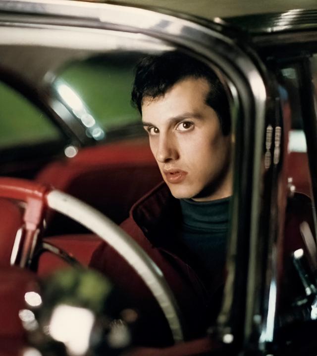 Großaufnahme von Arnie (Keith Gordon), der skeptisch blickend hinter dem Steuer eines Autos sitzt.