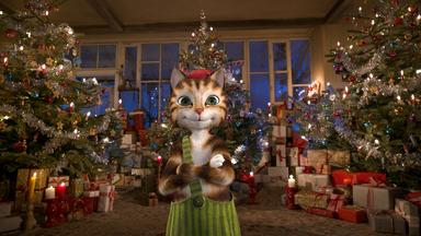 "Pettersson und Findus - Das schönste Weihnachtsfest überhaupt": Abend. Im Hintergrund eine Fensterfront, die das Zimmer der weihnachtlichen Bescherung abschließt. Wir sehen links, in der Mitte und rechts je einen riesigen, reich geschmückten Weihnachtsbaum, nach allen Seiten hin umlagert mit Bergen von Geschenken. Kerzen erzeugen ein warmes, freundliches Licht. Im Vordergrund steht Findus mit lässig verschränkten Armen und schaut den Betrachter selbstsicher und zufrieden an.