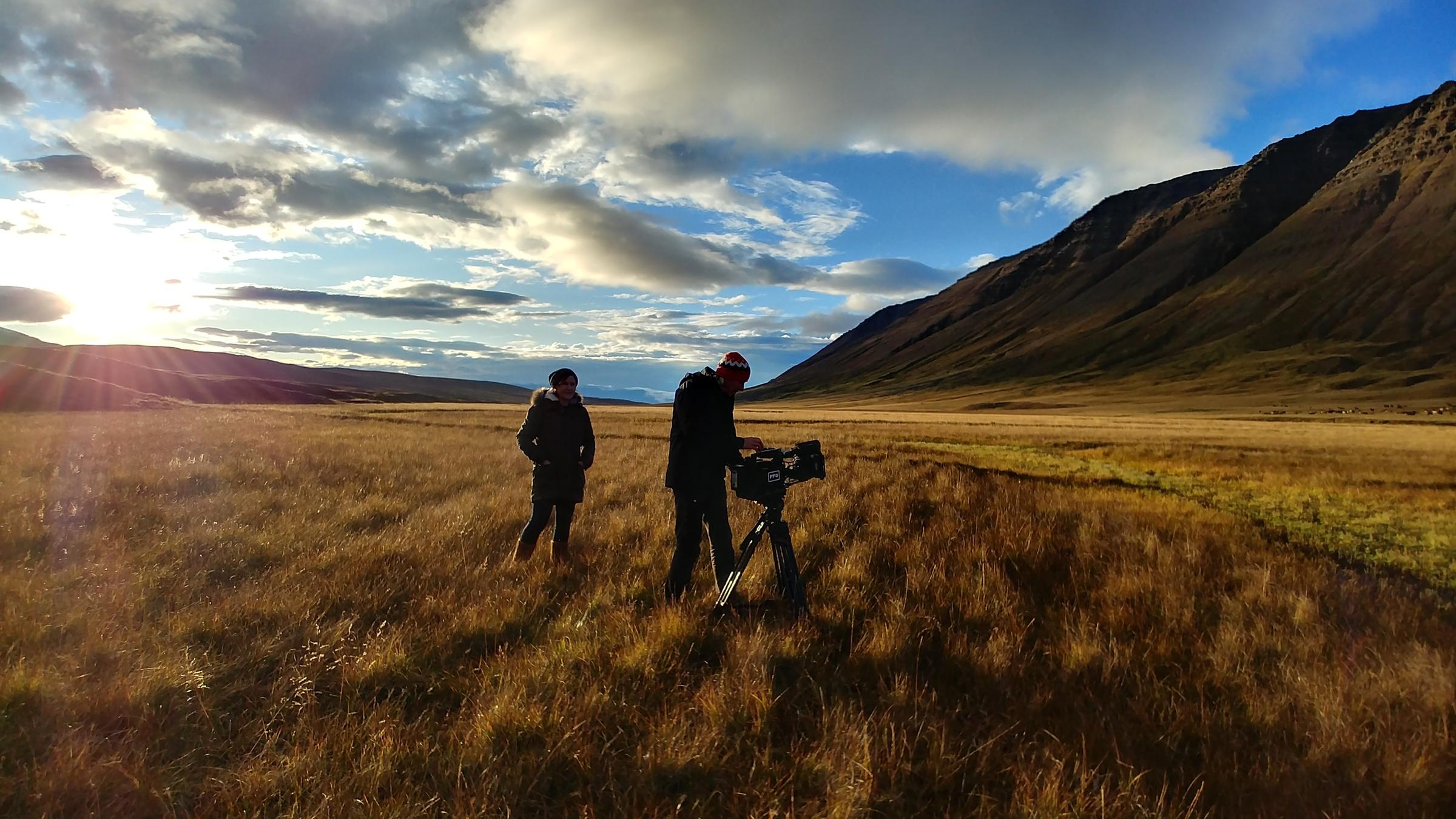 "Ausgerechnet Island: Leben zwischen Fjorden und Vulkanen": Weites Tal in herbstlichen Farben, am blauen Himmel türmen sich Wolken. Die Regisseurin Jeannine Apsel und Kameramann Florian Kössl stehen mit einer großen Kamera in der Mitte der großen Wiesen.
