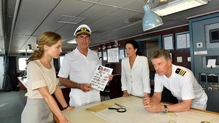 "Das Traumschiff: Hawaii": Kapitän Burger (Sascha Hehn), Hanna Liebhold (Barbara Wussow), Dr. Sander (Nick Wilder) und Katja (Hedi Honert) stehen zusammen um einen Tisch im Brückendeck. Vor ihnen liegt eine Landkarte ausgefaltet. Nachdenklich hält Kapitän Burger ein Erpresserschreiben in der Hand, dessen Wörter aus verschiedenen Buchstaben zusammengeklebt sind.