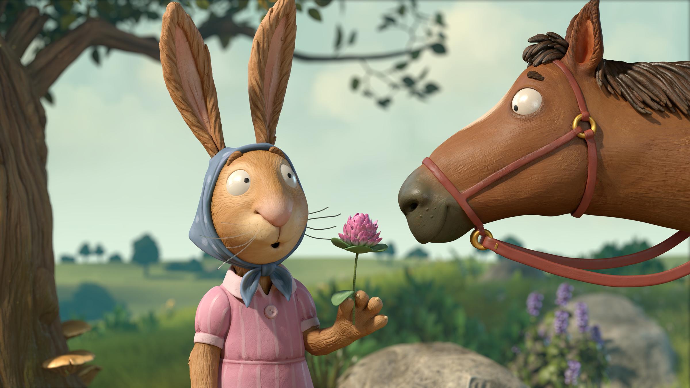 "Räuber Ratte": Auf einem Feldweg  steht Frau Hase  und hält einen einzigen Halm grünen, rosa blühenden Klee ausgestreckt in ihrer Hand. Das braune Pferd, das rechts neben ihr steht,  starrt hungrig auf den Halm Klee.