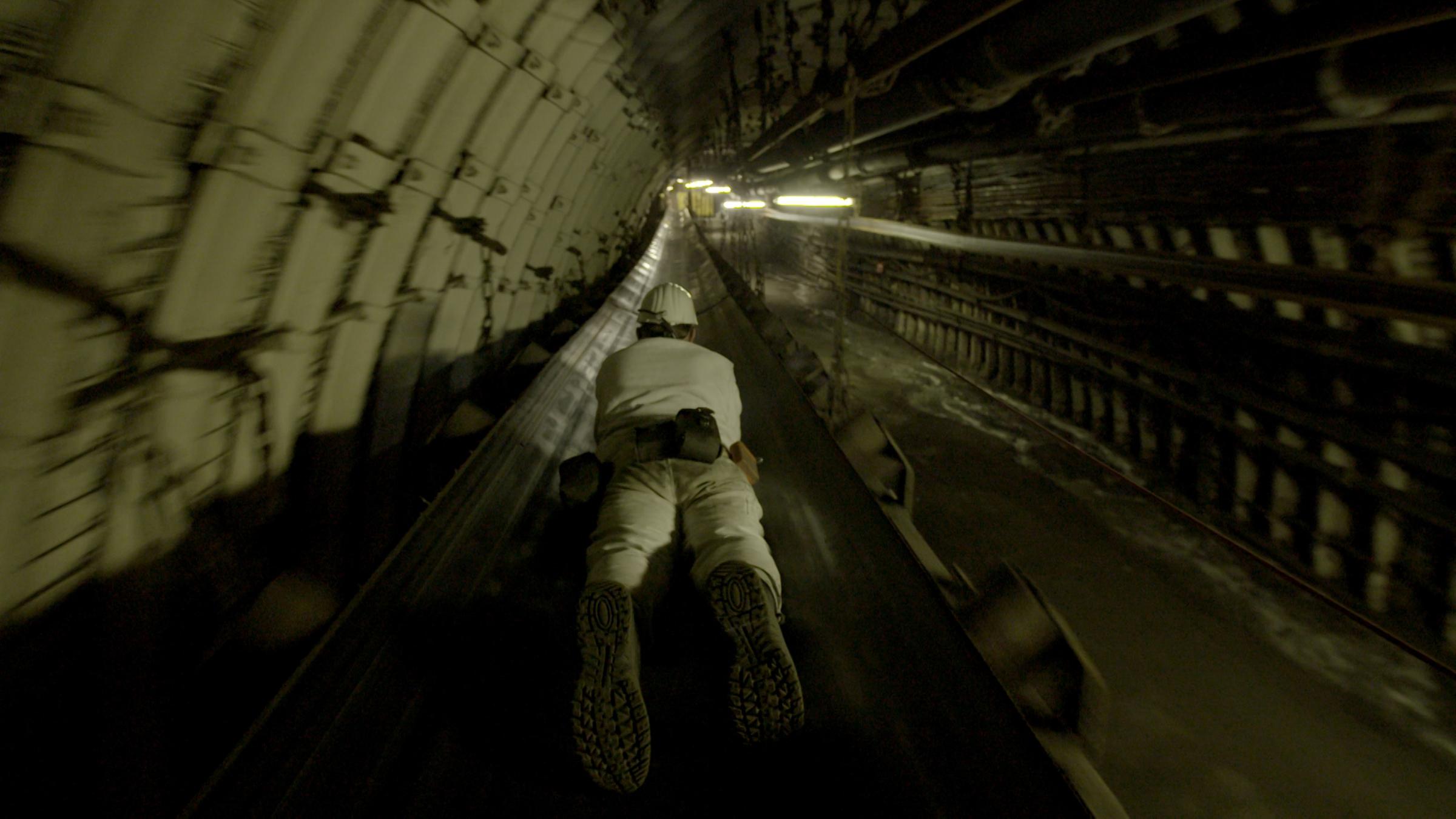 "Schwarzes Gold - Die Geschichte der deutschen Steinkohle" Ein Bergmann fährt - auf einem Förderband liegend - in einen Kohleschacht ein.