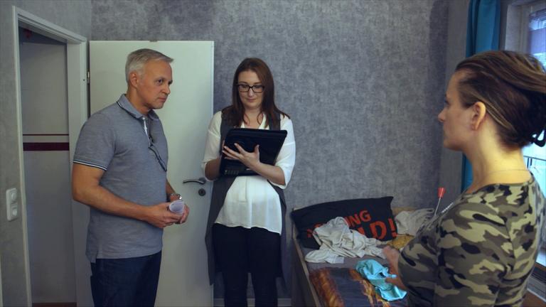 "Genug zum Leben? - Hartz IV auf dem Prüfstand": Jochen Knies und Sandra Dahms stehen mit einer jungen Frau in einem kleinen Zimmer. Sandra Dahms macht sich Notizen, während Jochen Knies die junge Frau ansieht, die seinen Blick erwidert.