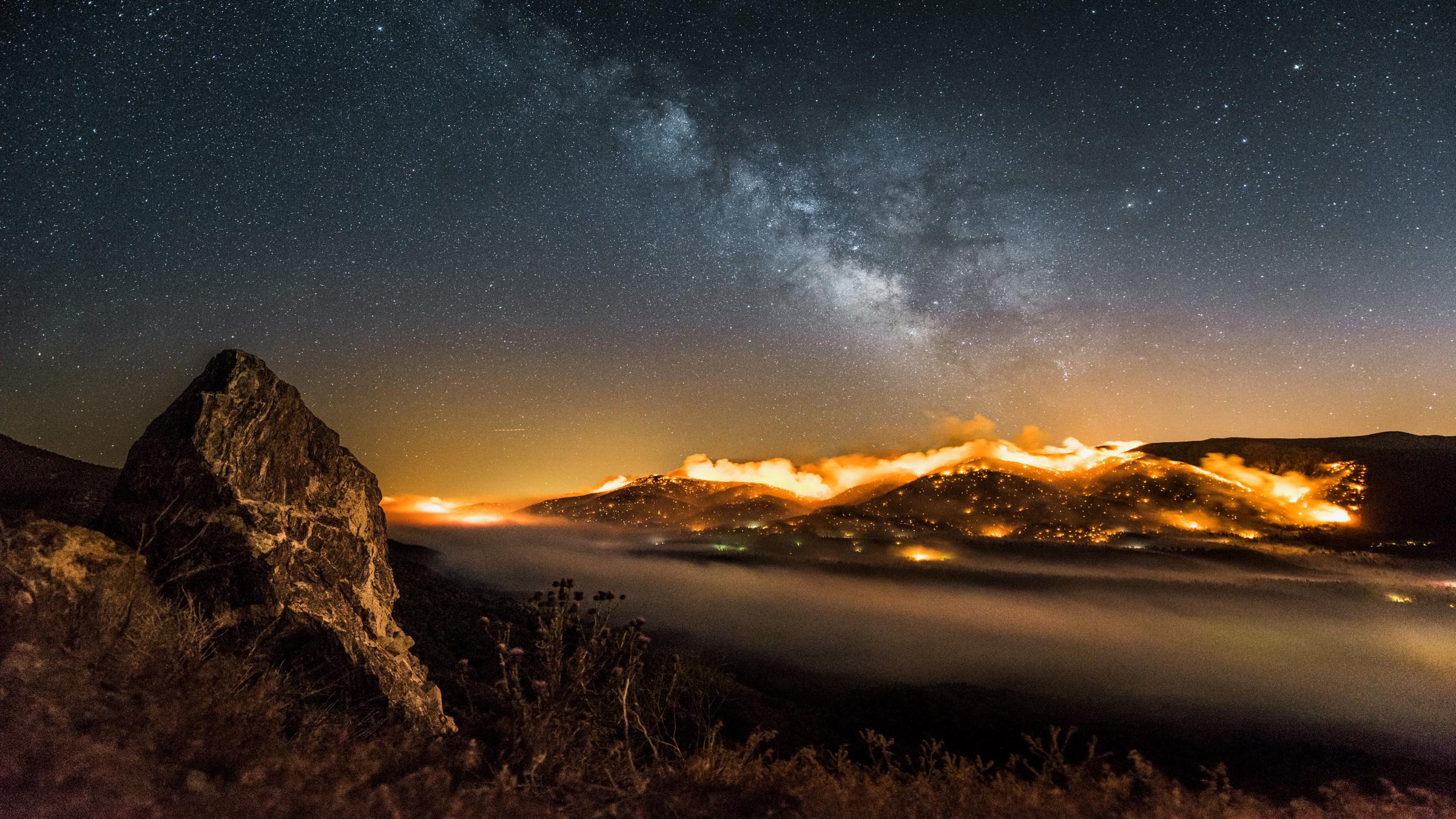 "One strange Rock - Unsere Erde: Atem": Zeitraffer-Aufnahme eines brennenden Hügels und darüber die Milchstraße.