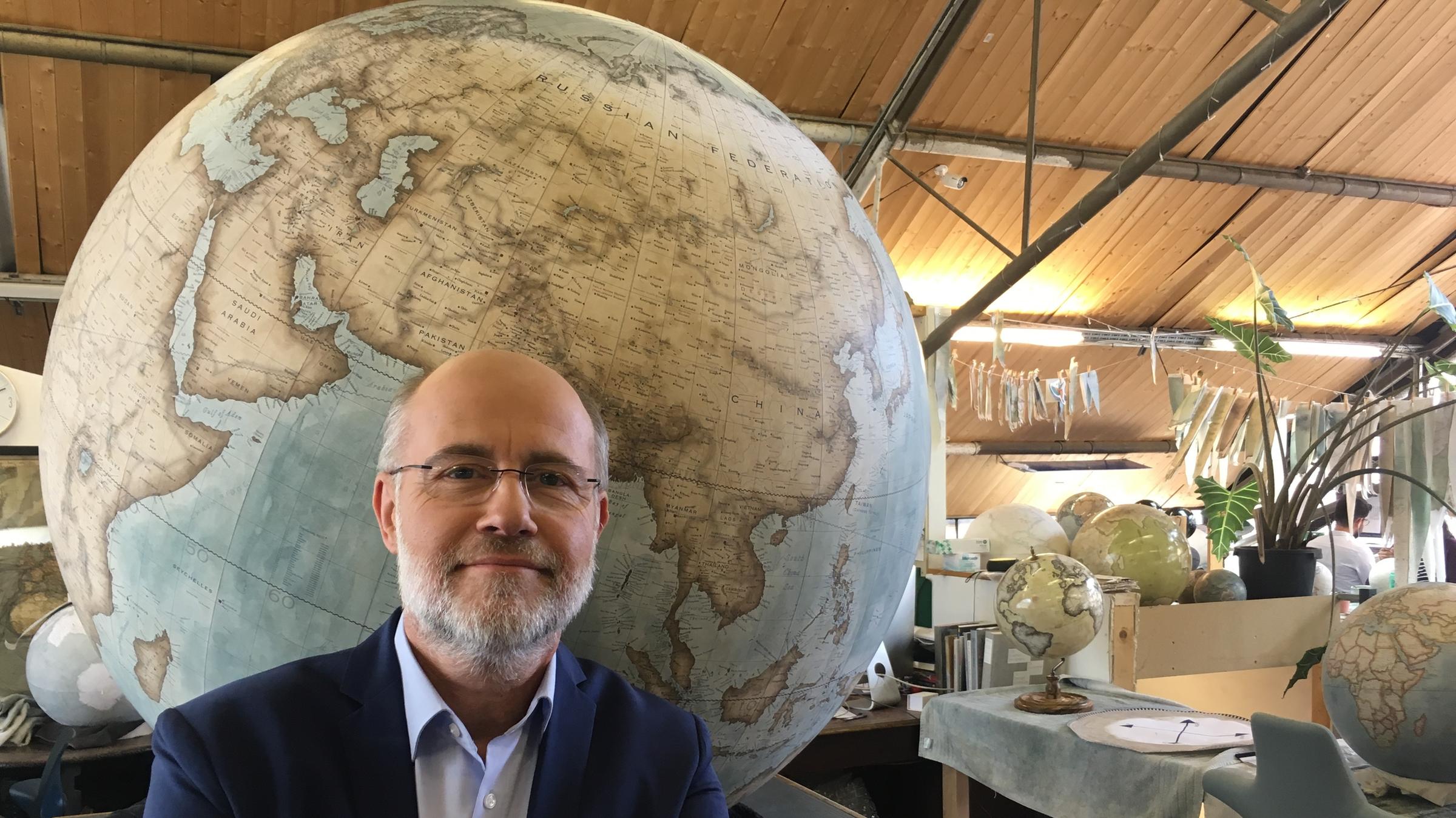 "Terra X: Die Vermessung der Erde: Von der Nebra-Scheibe bis zum GPS": Harald Lesch vor einem großen Globus. Er hat die Arme verschränkt und lächelt in die Kamera.