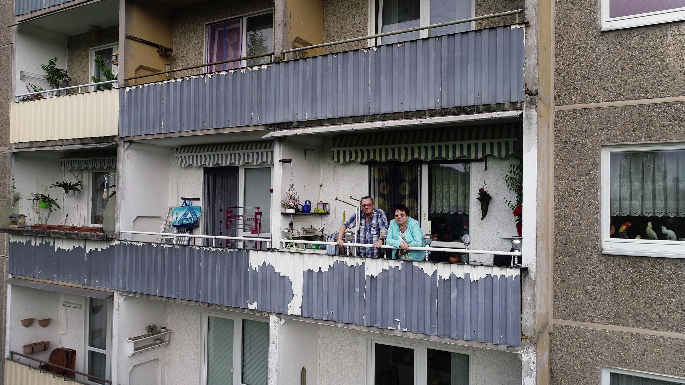 "37°: Plattgemacht - Wenn ein Stadtteil verschwindet": Christine und Hans stehen auf einem Balkon einem Plattenbau. Das Gebäude wirkt verfallen, die Farbe blättert von der Fassade.