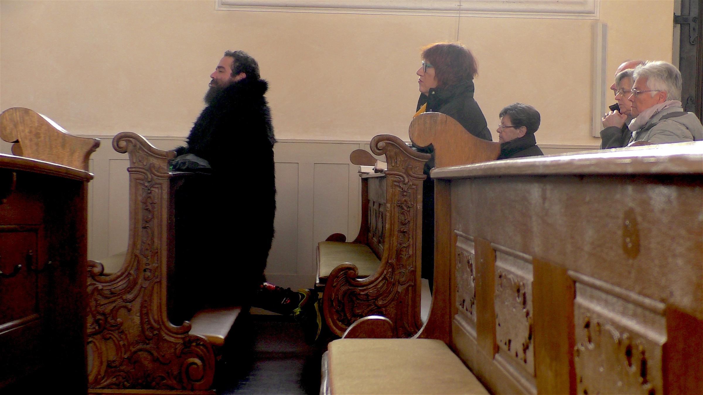 "Ach, du liebes Abendland - Ein Syrer erkundet seine deutsche Heimat": Firas Alshater ist während eines Gottesdienstes in einer Kirche. Er kniet betend nieder.