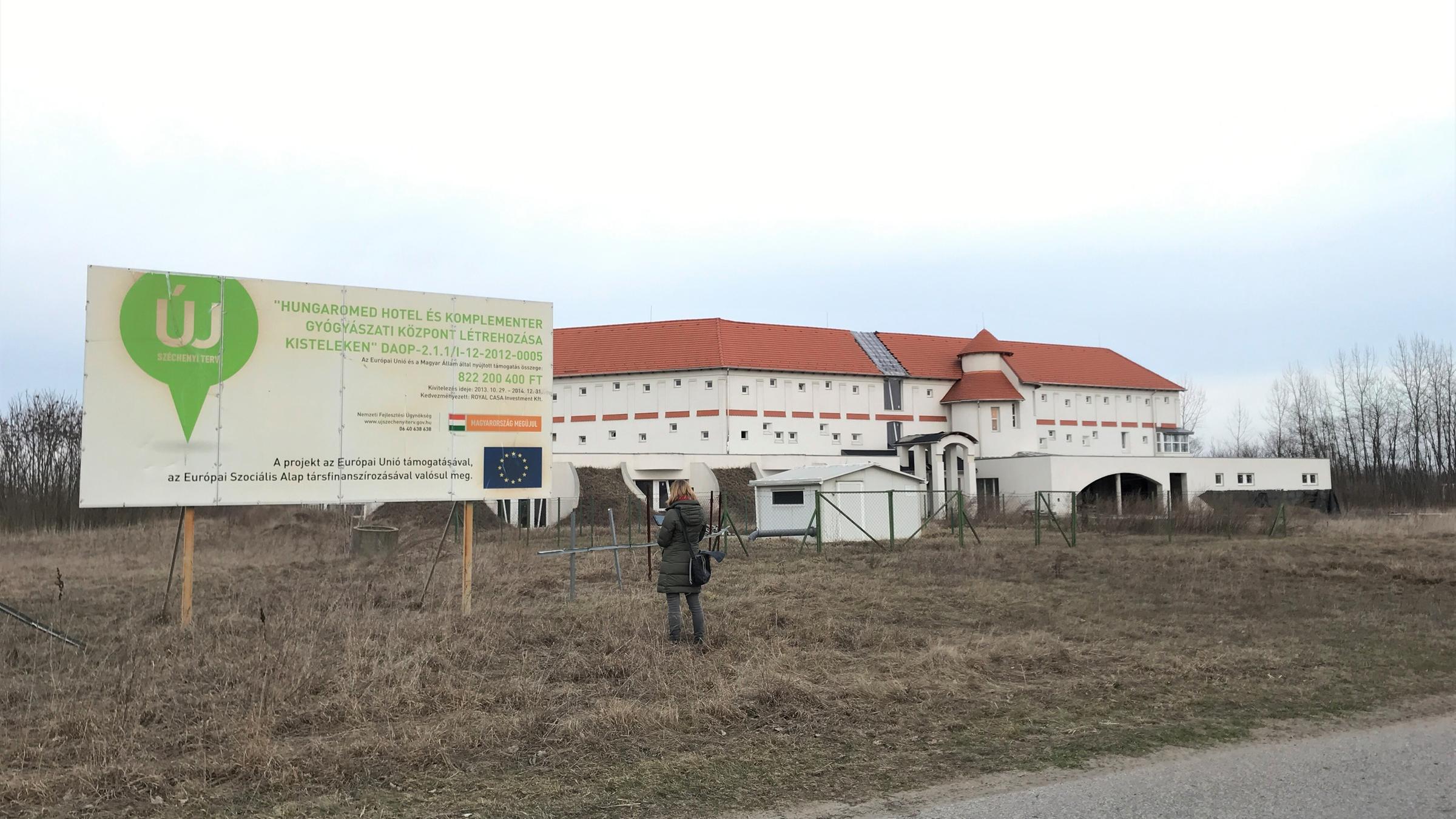 "ZDFzoom: Betrügen leicht gemacht": Frau steht vor einer Hinweistafel. Im Hintergrund sieht man ein Gebäude.