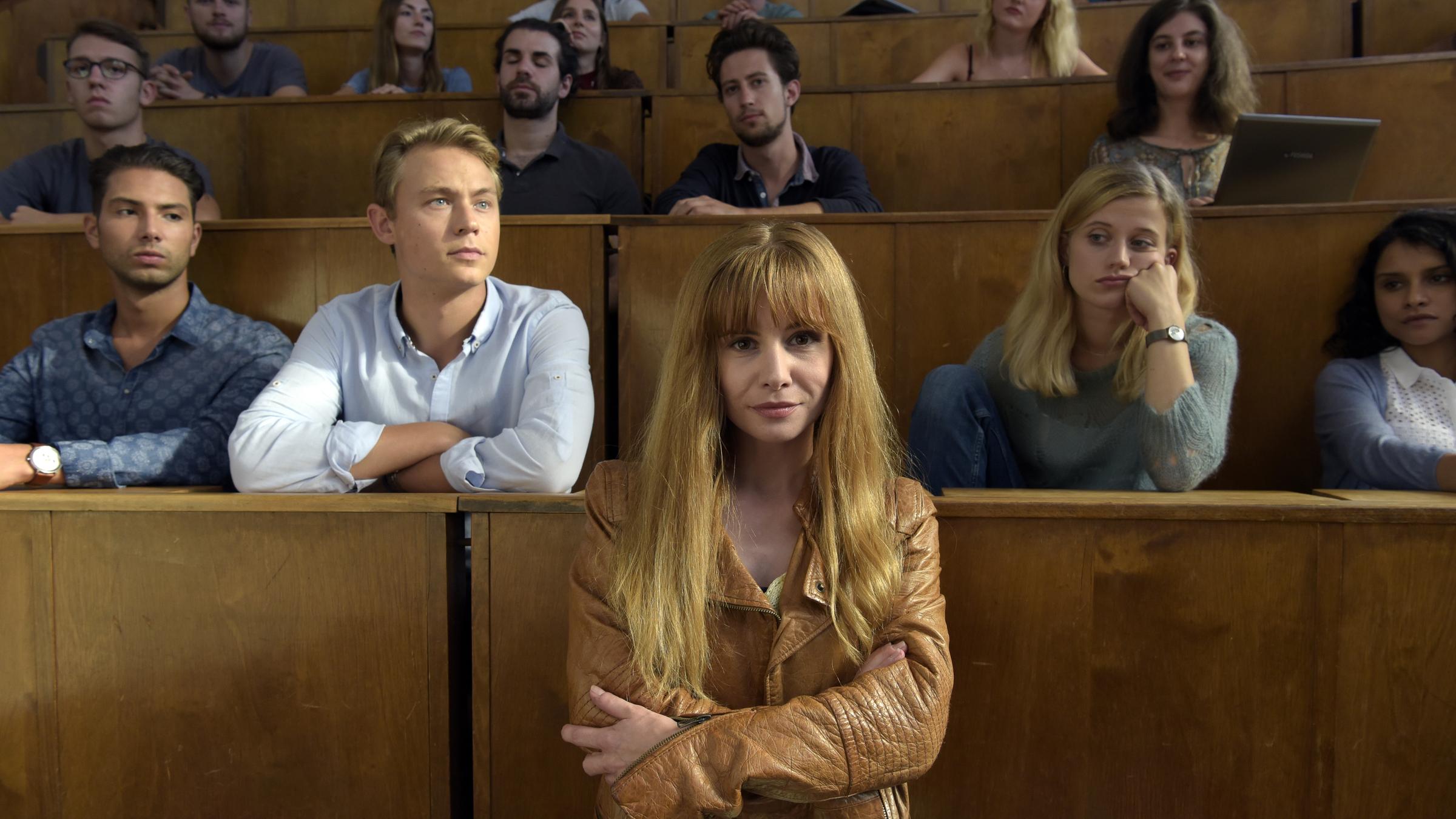 "Lotta & der schöne Schein": Lotta (Josefine Preuß) steht in einem Hörsaal in der Uni. Danny (Dennis Mojen) und Magda (Camille Dombrowsky) sitzen zusammen mit anderen Studenten hinter ihr.