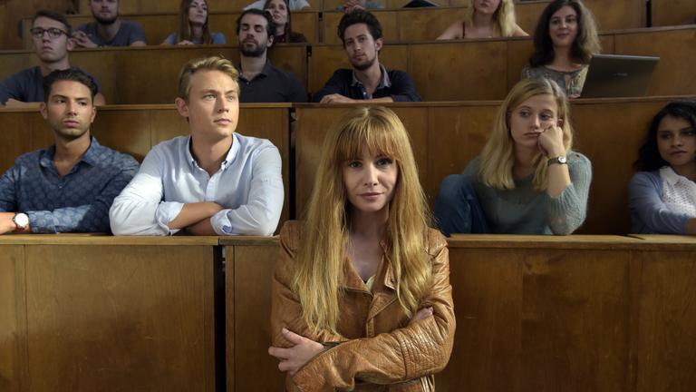 "Lotta & der schöne Schein": Lotta (Josefine Preuß) steht in einem Hörsaal in der Uni. Danny (Dennis Mojen) und Magda (Camille Dombrowsky) sitzen zusammen mit anderen Studenten hinter ihr.