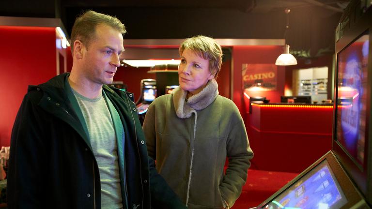 "Marie Brand und das Spiel mit dem Glück": Die beiden Kommissare stehen vor einem Spielautomaten im Spielcasino. Jürgen Simmel bedient den Automaten und Marie Brand schaut ihn verwundert an.