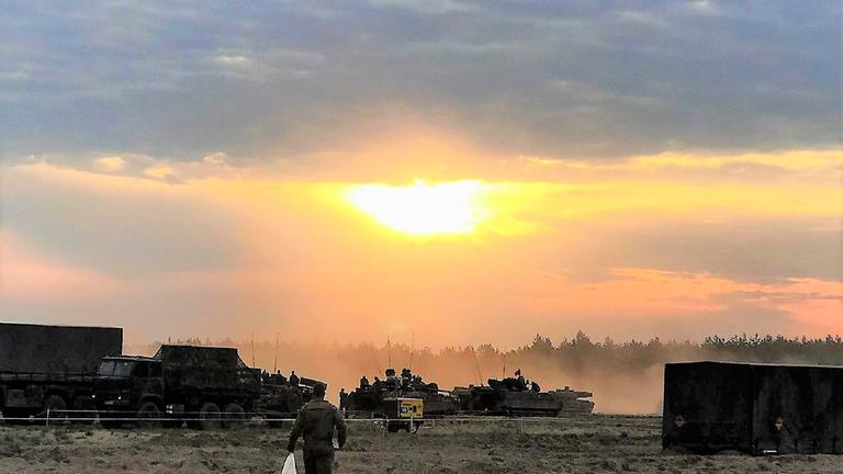 "Alte Bündnisse - neue Bedrohungen: Deutschlands Rolle in der NATO und der Welt": Ein Soldat geht im Licht der Abendsonne auf eine Reihe von Fahrzeugen und Panzern zu.