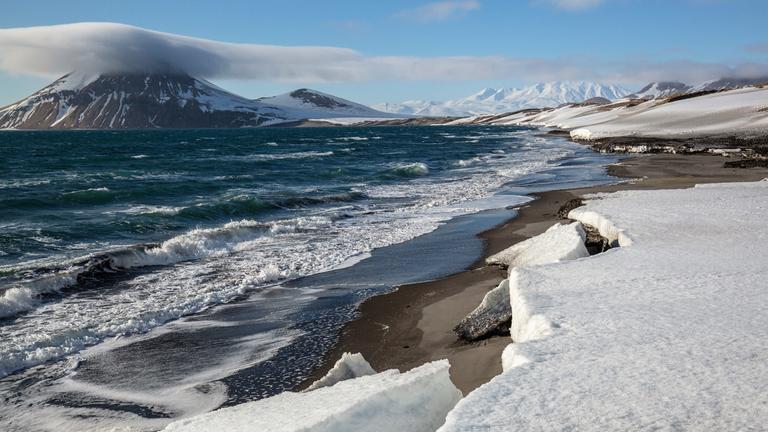 "Terra X: Wale, Robben, Riesenbären - Das Ochotskische Meer": Meer und Küste, teilweise mit Schnee und Eis bedeckt, links im Hintergrund wolkenverhangener Vulkan.