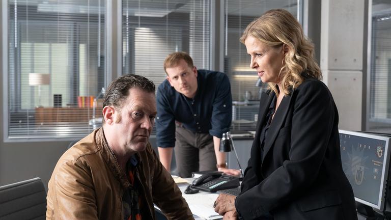 Die Chefin - Justitias Zuhälter“: Vera Lanz (Katharina Böhm) sitzt auf der Tischkante Paul Böhmer (Jürgen Tonkel) gegenüber. Maximilian Murnau (Christoph Schechinger) stützt sich zwischen den beiden auf dem Tisch auf.