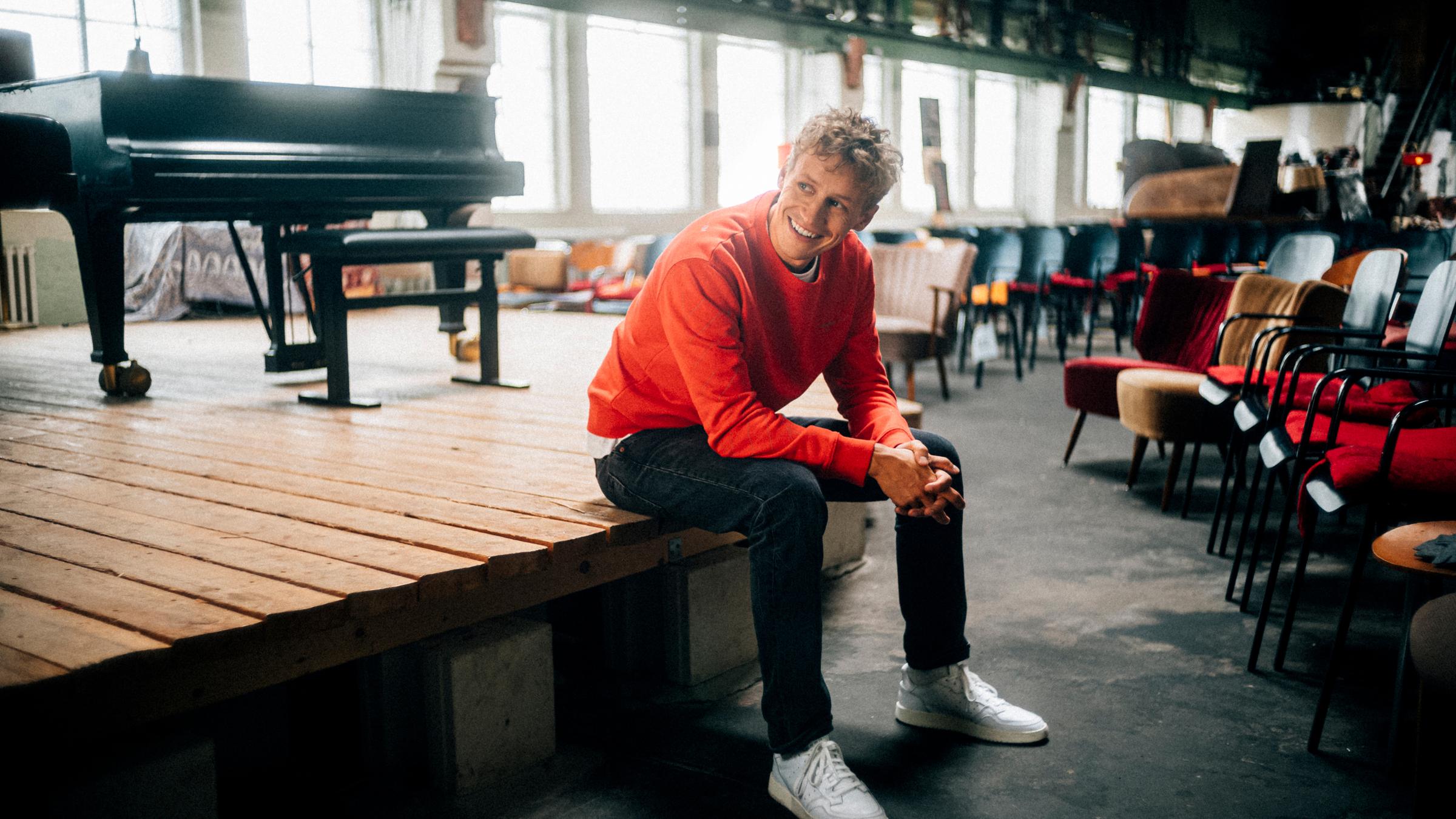 "Weihnachten in Rom": Der Sänger Tim Bendzko sitzt am Rand einer hölzernen Bühne in einer als Konzertsaal genutzten Fabrikhalle. Auf der Bühne steht ein Flügel. Im Hintergrund Stuhlreihen.