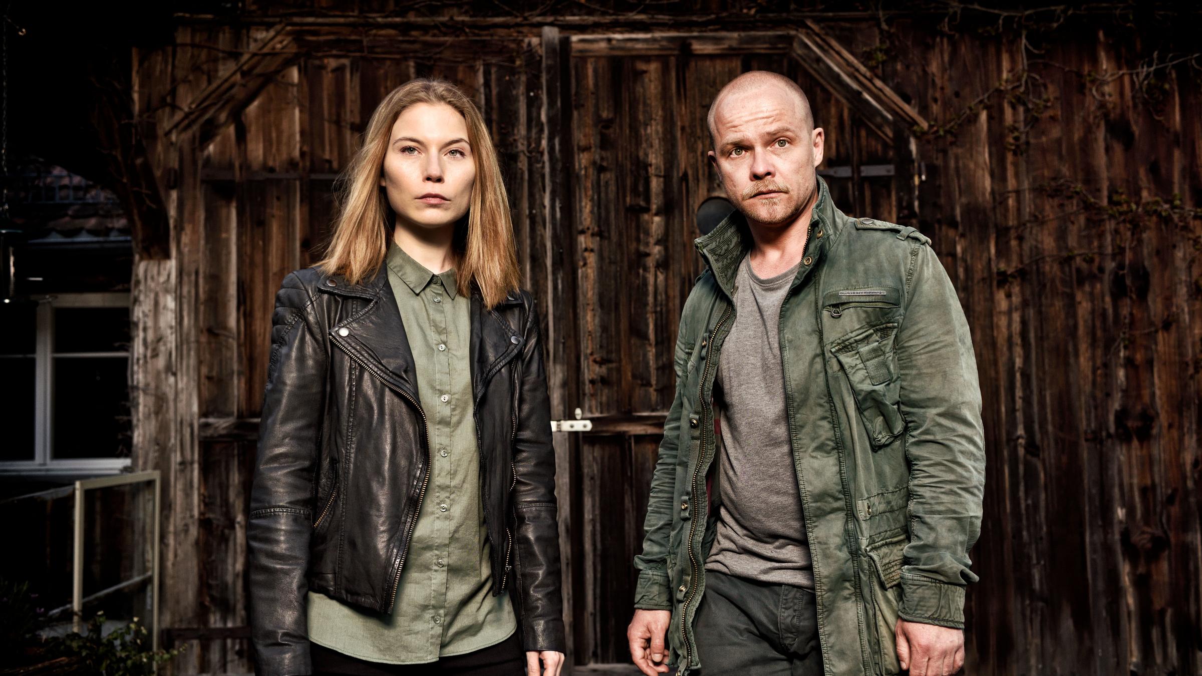 „Die Toten vom Bodensee - Der Stumpengang“: Hannah Zeiler (Nora Waldtstätten) und Micha Oberländer (Matthias Koeberlin) stehen nebeneinander vor einem dunklen Holztor.