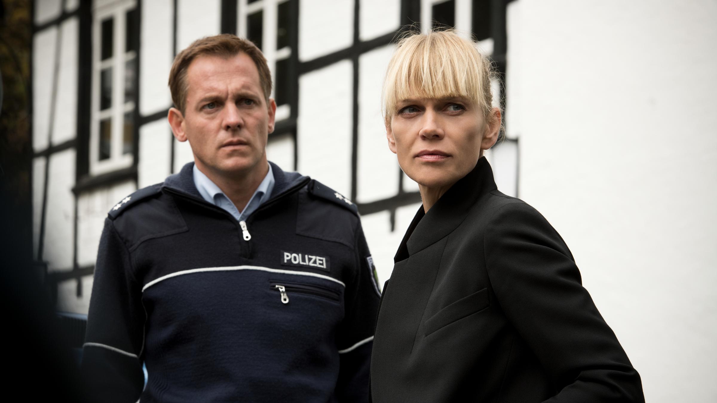 „Helen Dorn – Nach dem Sturm“: Tom Petersen (Johannnes Zirner) und Helen Dorn (Anna Loos) stehen nebeneinander im Freien vor einem weißen Haus.