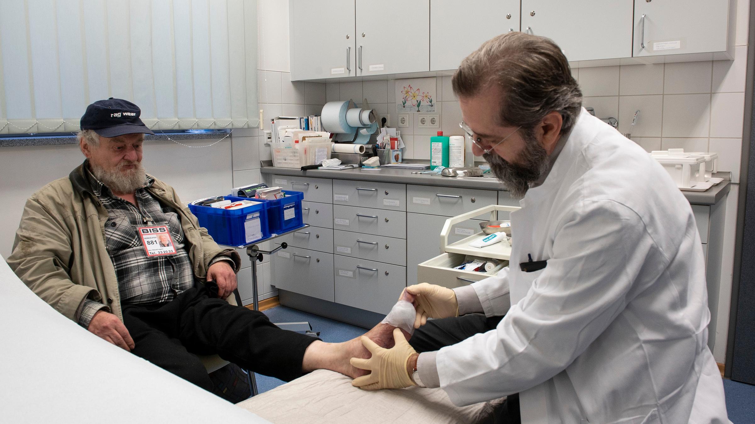  "37°: Wo andere wegsehen - Ärzte im Einsatz für Obdachlose":  Dr. Thomas Beutner betrachtet den Fuß eines alten Mannes, der vor ihm sitzt, in einem Arztzimmer.