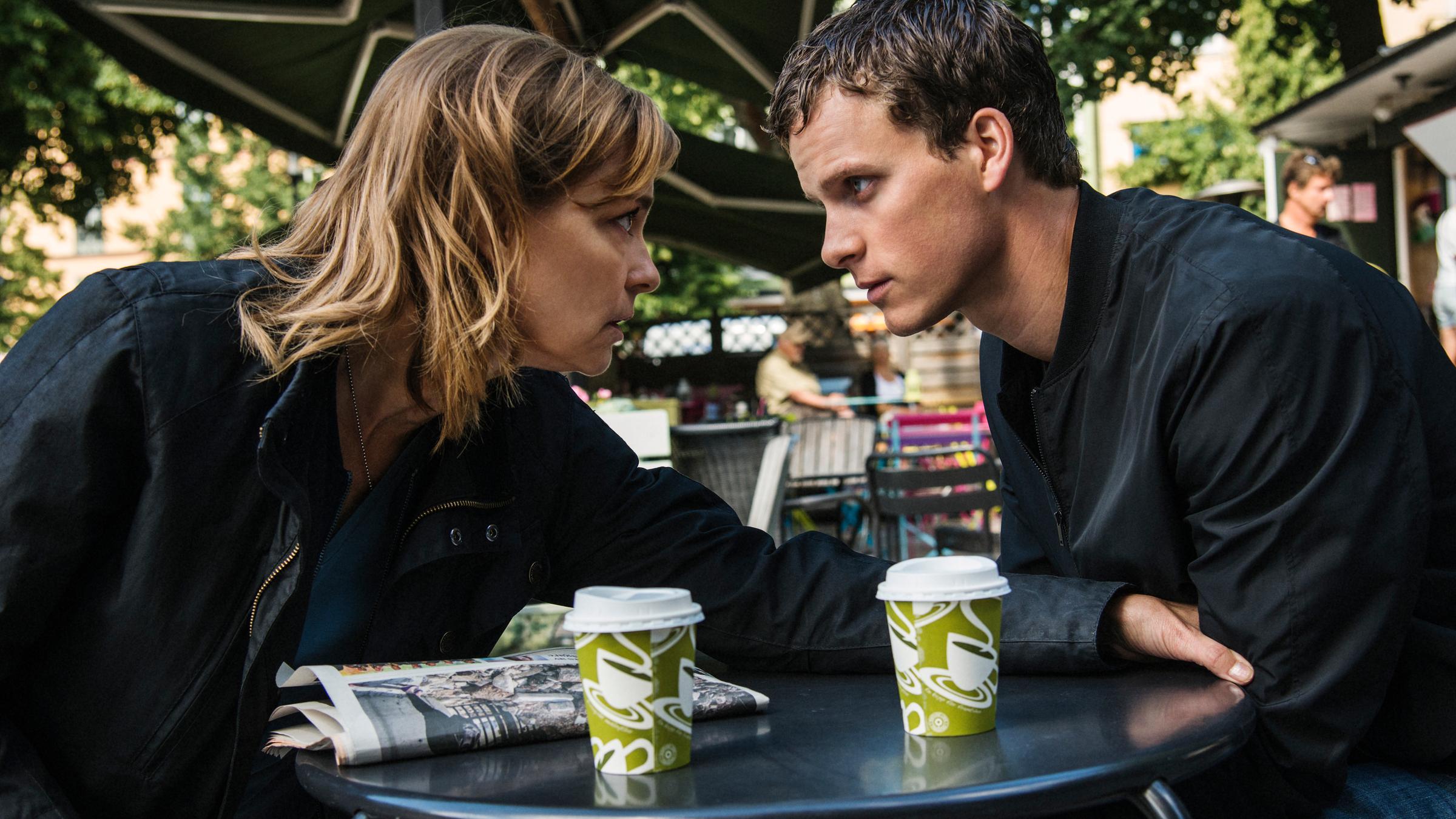 "Hanna Svensson - Blutsbande": Hanna Svensson (Marie Richardson) und Christian (Adam Pålsson) sitzen an einem Tisch vor einem Café und unterhalten sich.