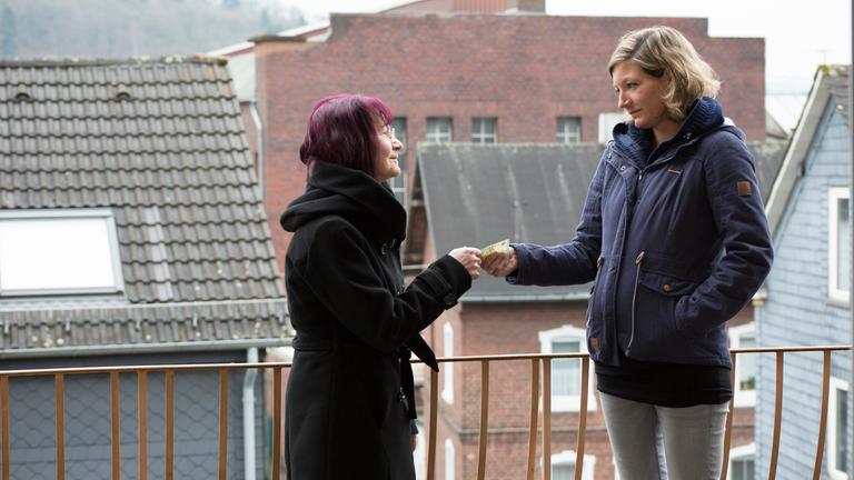 "37°: Meine Mutter, mein Sorgenkind - Wenn die Rente nicht reicht": Giesela und Christiane stehen auf einem Balkon. Im Hintergrund sind Wohnhäuser zu sehen. Christiane reicht Giesela einen Geldschein.