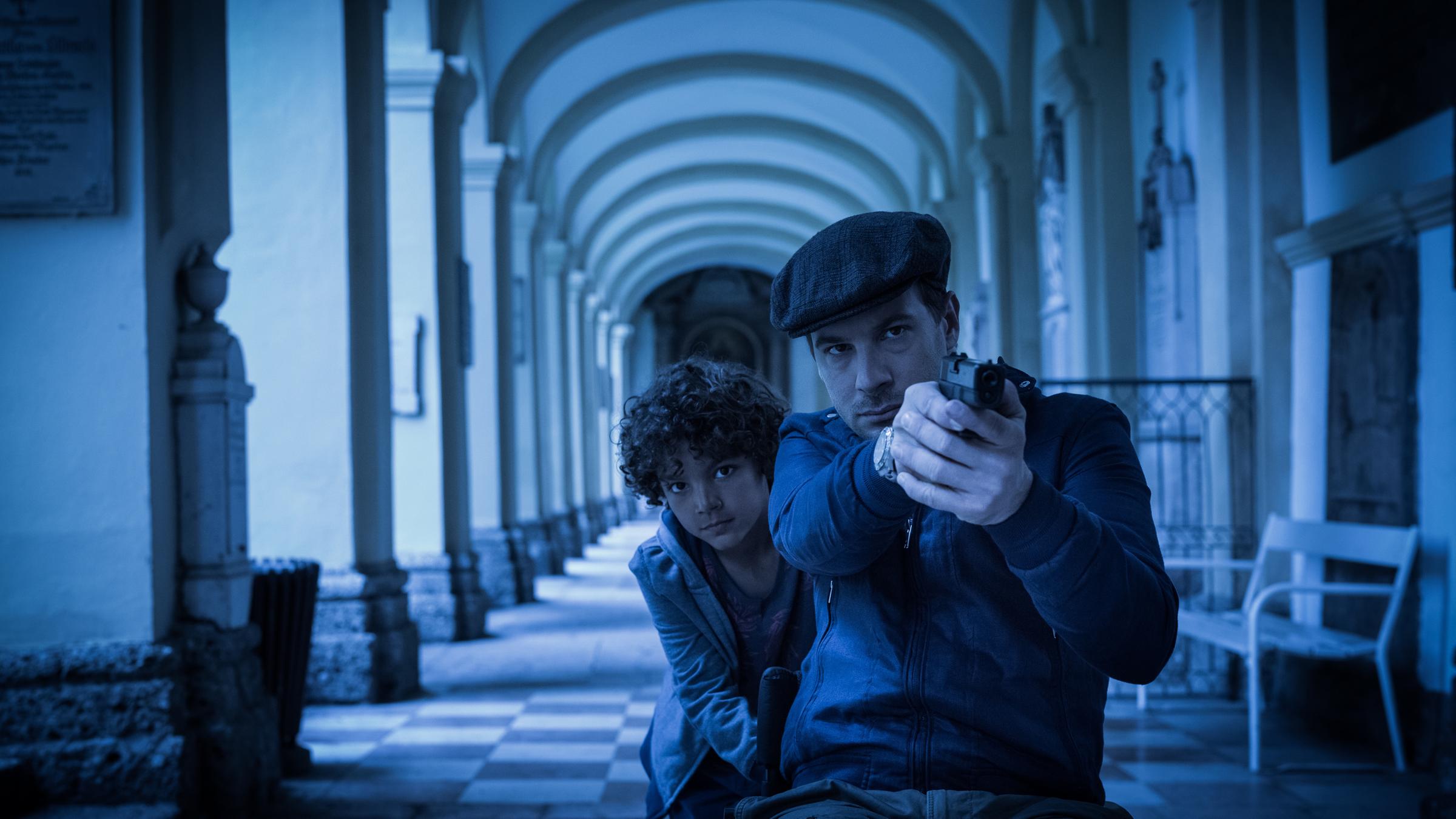 „Die Toten von Salzburg  - Königsmord“:  Major Peter Palfinger (Florian Teichtmeister) mit gezogener Waffe in einem dunklen Gewölbegang, hinter ihm duckt sich Tyki (Adrian/Marius Maier).