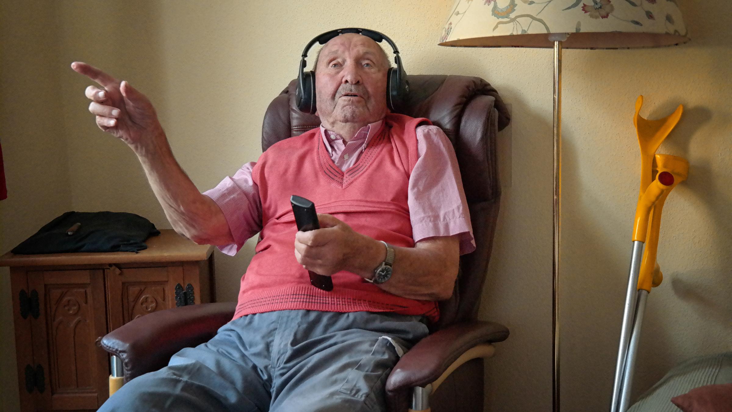 "37° - Mit 100 ist noch nicht Schluss: Alt aber nicht von gestern": Herr Körber sitzt im Sessel und hat Kopfhörer auf. In seiner rechten Hand hält er die Fernbedienung für das Fernsehgerät.