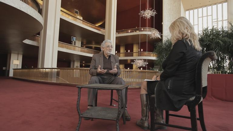"Stars gegen Trump - Widerstand in New York?": Der Tenor Placido Domingo sitzt in einem Sessel im Foyer der Metropolitan Opera und spricht mit der Filmemacherin, die ihm gegenüber sitzt. Im Hintergrund das prachtvolle Treppenhaus der Oper.