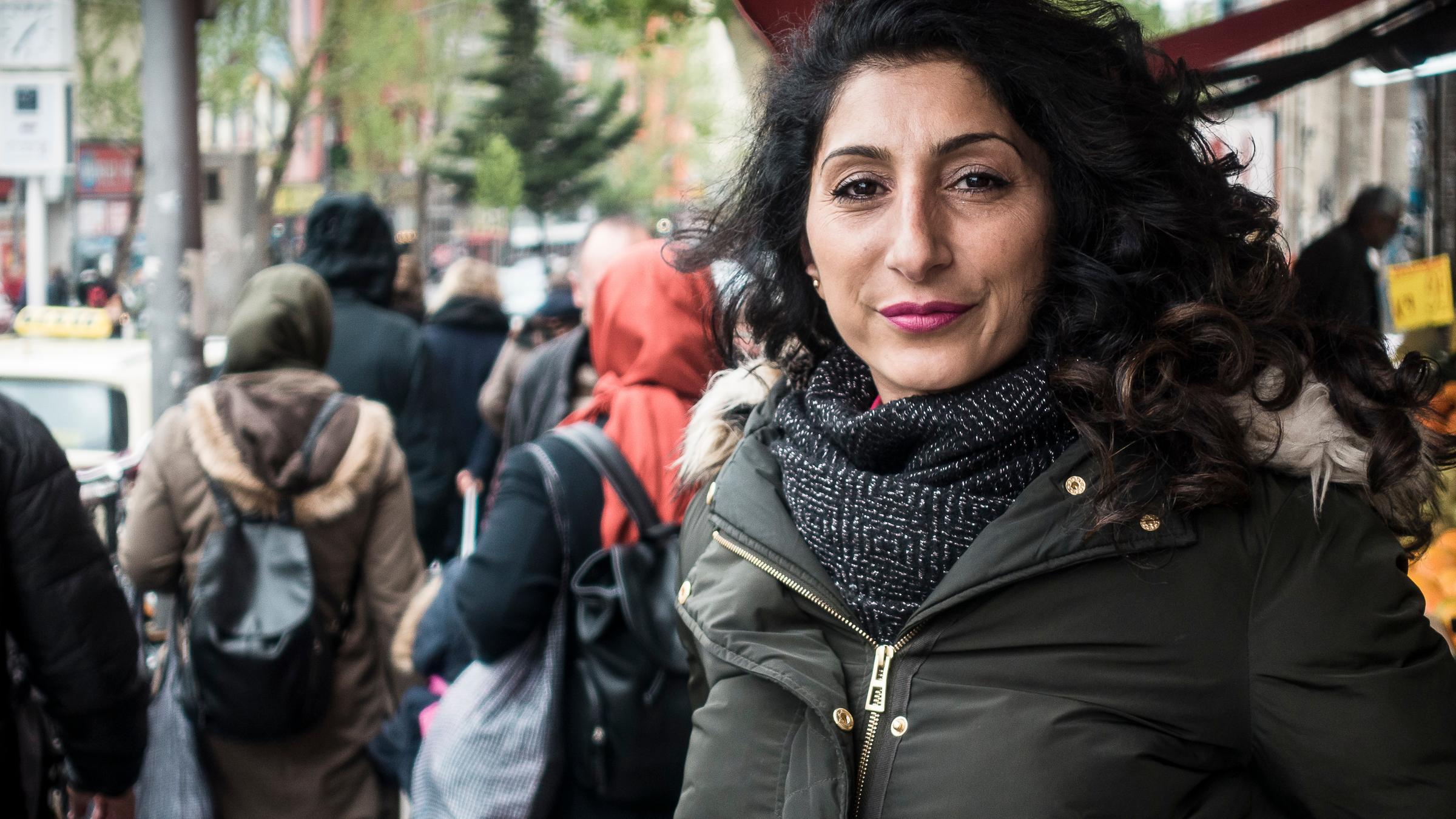 "37°: Im Schatten der Clans - Eine Frage der Ehre": Die 44-jährige türkischstämmige Sozialarbeiterin Songül Ç. steht auf einer belebten Geschäftsstraße in Berlin-Neukölln und blickt selbstbewusst in die Kamera. In der linken Bildhälfte von hinten zu sehen: zwei Frauen mit Kopftüchern.