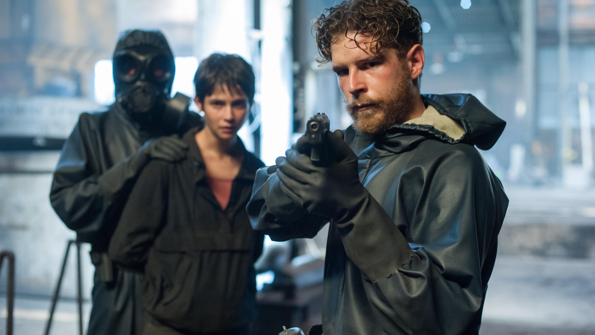 "La Zona - Do not cross (1)":  Martín (Álvaro Cervantes, r.) steht mit gezogener Waffe vor der festgenommenen, im Hintergrund stehenden Schmugglerin Zoe (Alba Galocha, Mitte).