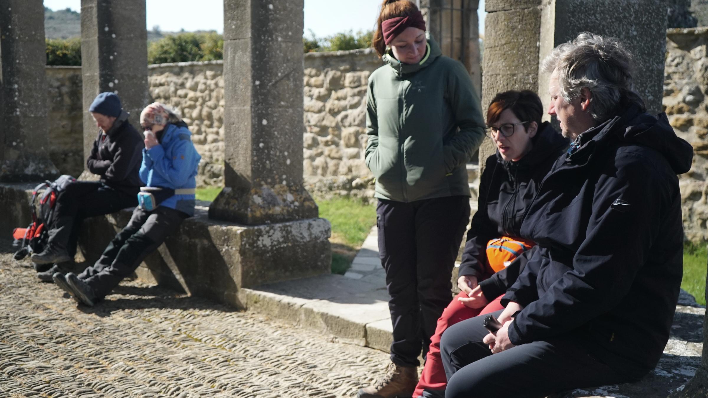"Mein härtester Weg - Pilgern nach Santiago de Compostela": Außenaufnahme - Drei Frauen und zwei Männer machen Rast an einer alten Kirche. Sie sitzen auf den Sockelmauern der Säulen.