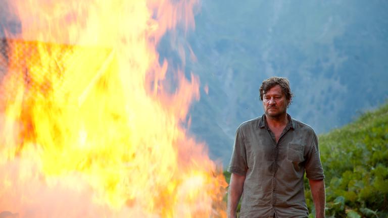"Endabrechnung": Severin Verginer (Harald Windisch) steht neben einem großen Feuer, im Hintergrund ist ein Feld zu sehen.
