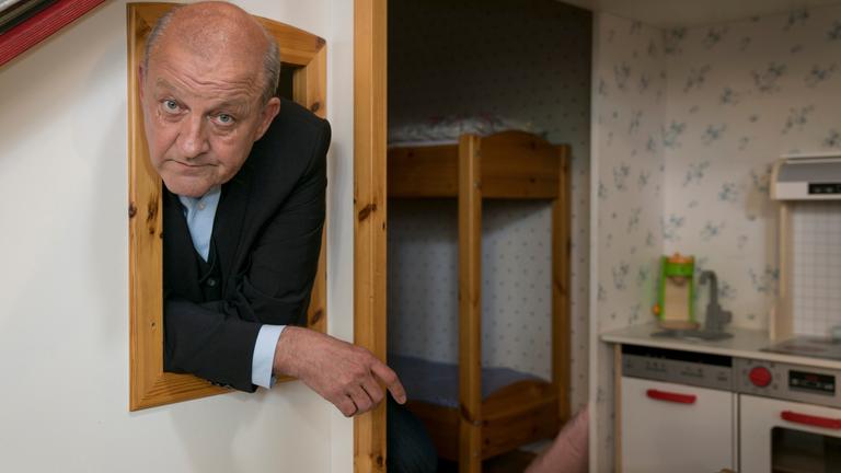 „Wilsberg - Minus 196°“: Georg Wilsberg (Leonard Lansink) lehnt sich aus dem Fenster einer Puppenstube.