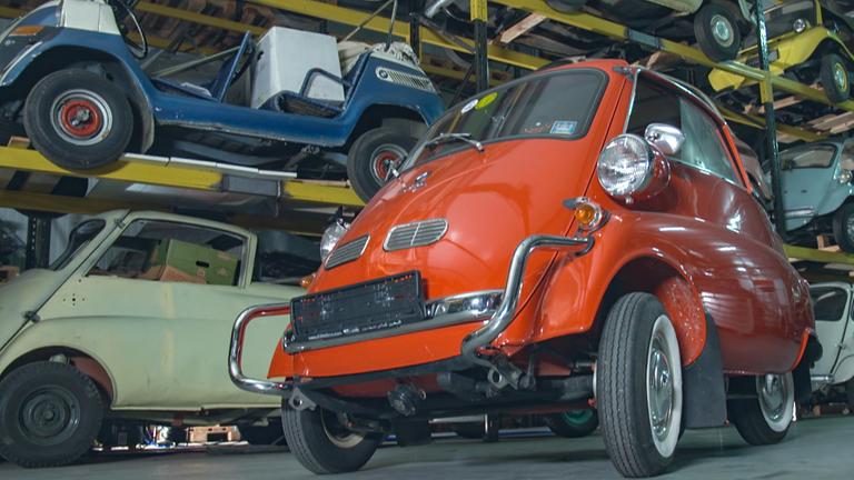 "Bella Germania - Die Dokumentation": BMW Isetta in einer Halle. Im Hintergrund in einem Hochregal weitere Fahrzeuger dieses Typs.