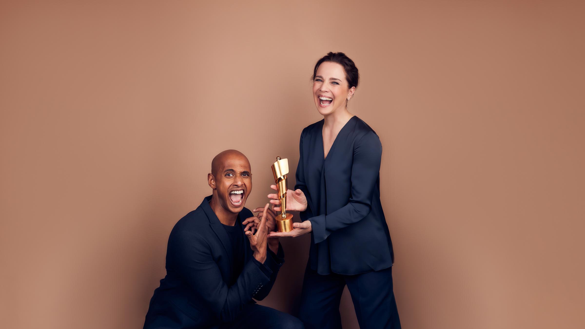 "Deutscher Filmpreis 2019": Teddy Teclebrhan und Désirée Nosbusch. Sie hält den Filmpreis in ihren Händen, er zeigt darauf, beide lachen in die Kamera.