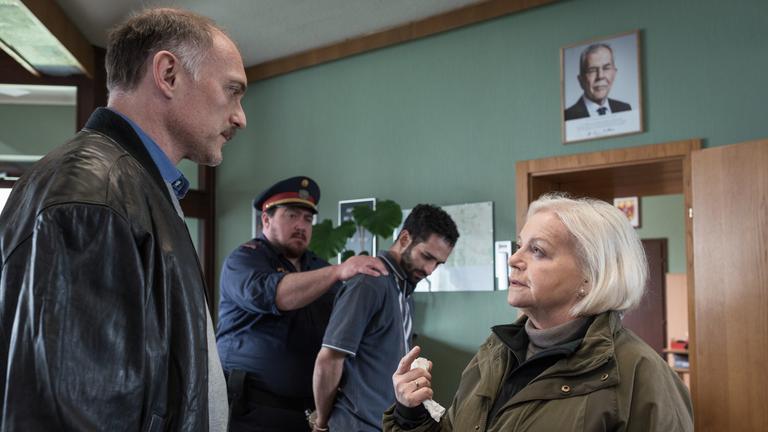 "Grenzland - Landkrimi": Achmet (Hassan Akkouch) wird von Hans Boandl (Christoph Krutzler) abgeführt. Vor ihnen im Zimmer stehen sich Elfriede Jandrasits (Brigitte Kren) und Dr. Schneider (Markus Schleinzer) gegenüber und unterhalten sich.