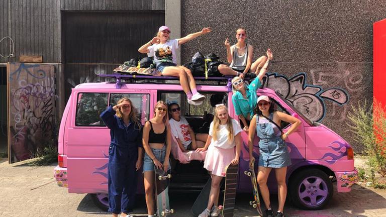 "Ab 18! - Skater Girls": Eine Gruppe junger Frauen steht vor einem rosa Bus.