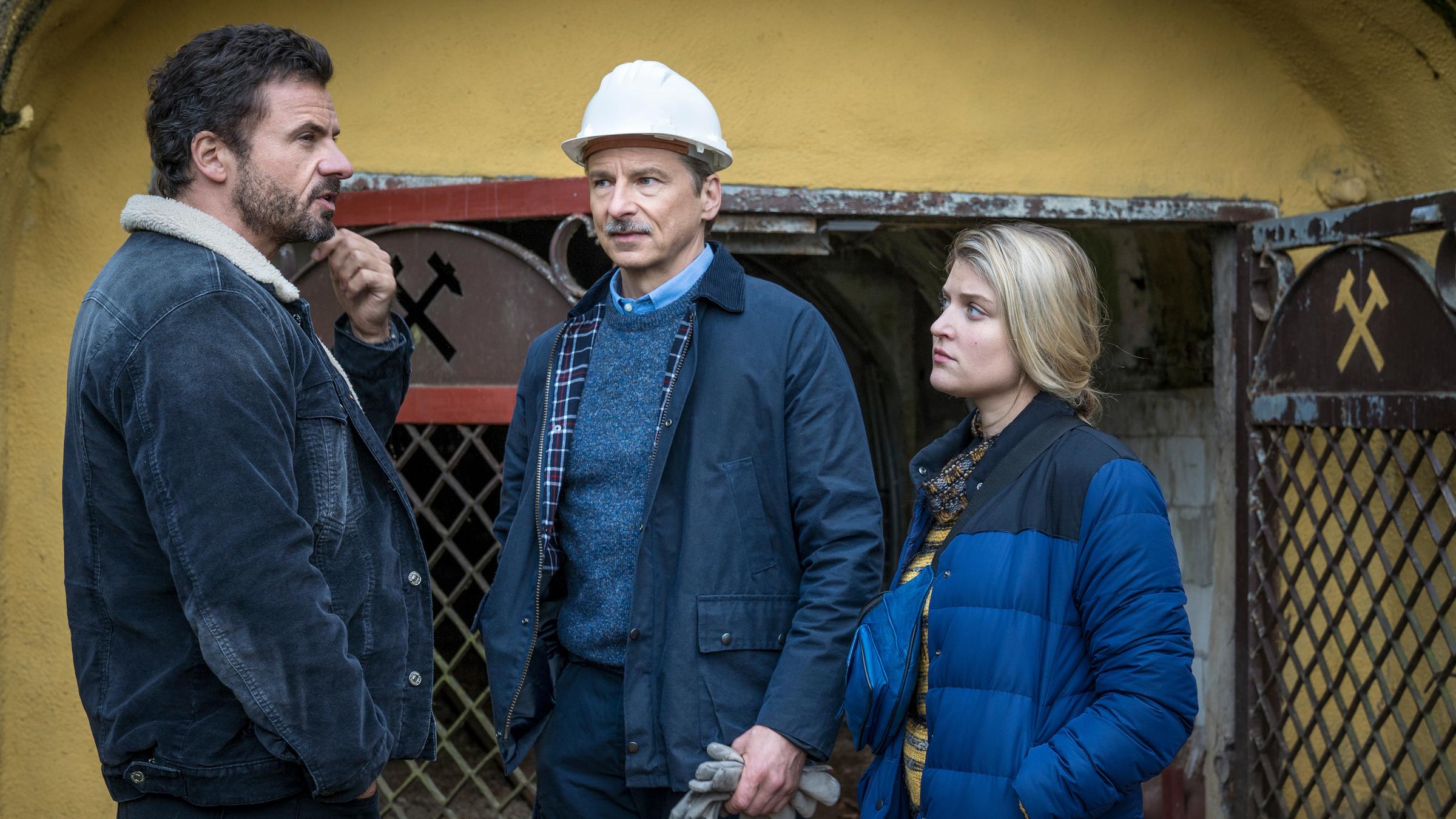 "Erzgebirgskrimi – Der Tote im Stollen": Adam (Stephan Luca) und Karina (Lara Mandoki) stehen zusammen mit Knut Erichsen (David Bunners) vor dem Eingang zu eines Stollens. Erichsen und Karina schauen zu Adam, der nachdenklich in die Ferne blickt.